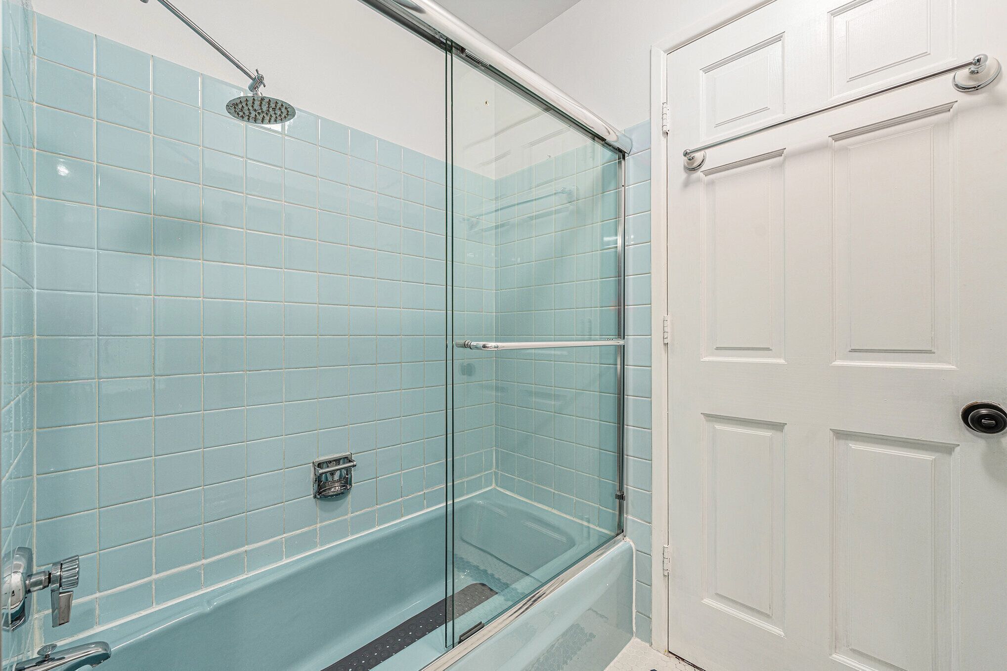 Un baño con ducha de vidrio, una puerta blanca y azulejos azul claro.