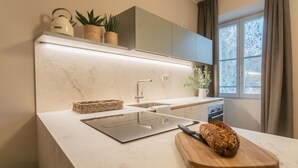 A modern kitchen with a marble countertop, a bread loaf on a wooden cutting board, and a kettle on the shelf. - V Suite on Lake Como (Como)