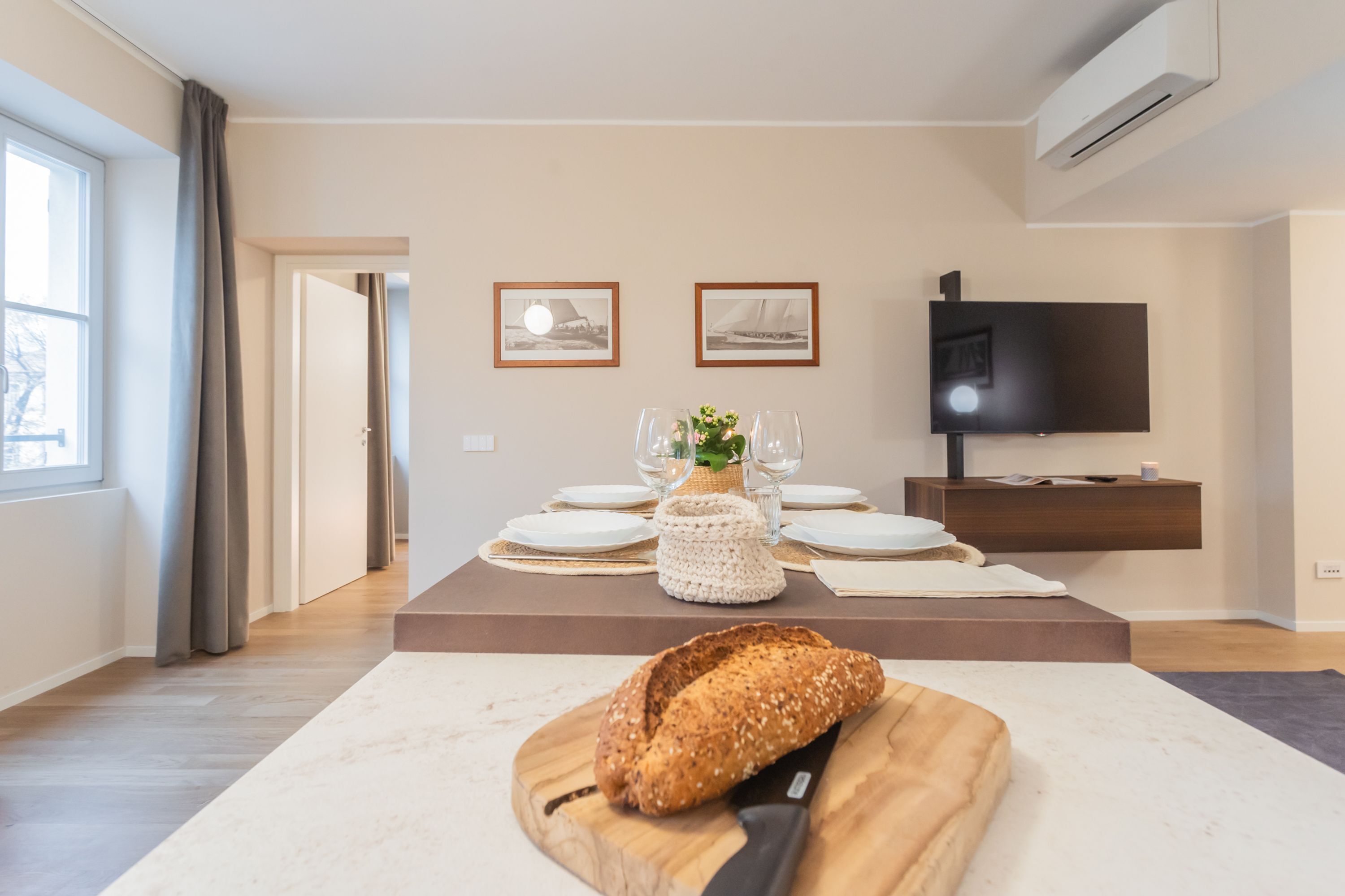 Un soggiorno moderno con zona pranzo, televisore piatto a parete e un'ampia finestra con tende.