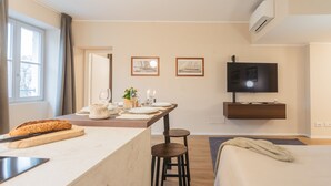 A modern hotel room with a kitchen area, a dining table set with plates and glasses, a bed with a blanket, and a mounted TV. - V Suite on Lake Como (Como)