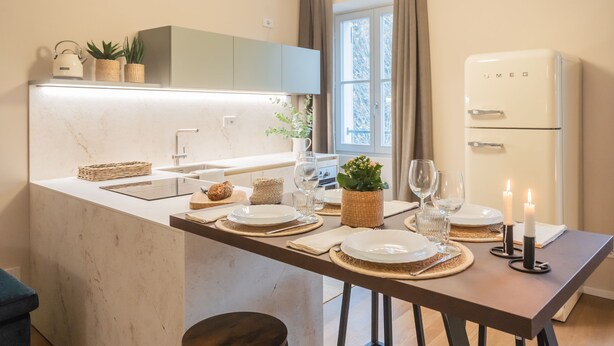 A modern kitchen with a marble countertop, a built-in oven, and a dining area set with plates, glasses, and candles. - V Suite on Lake Como (Como)