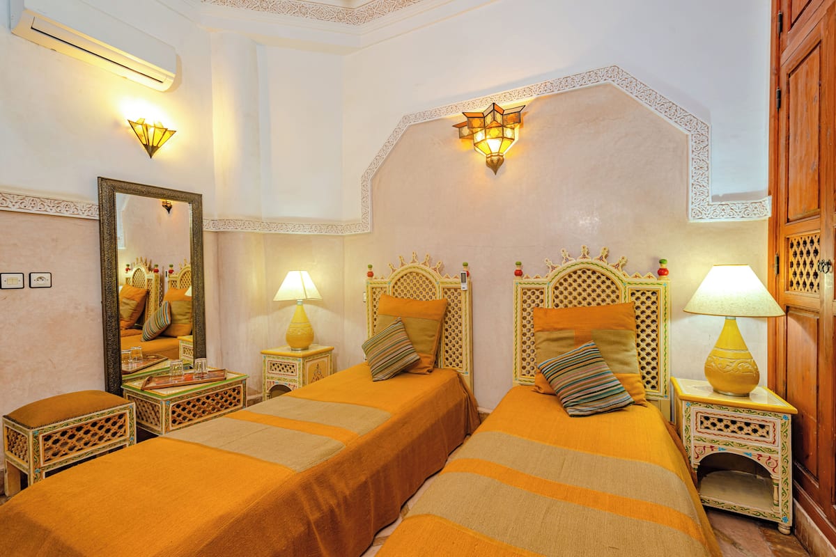 Une chambre d’hôtel avec deux lits, chacun doté d’une tête de lit et d’un pied de lit assortis, d’un grand miroir et de deux lampes de chevet.