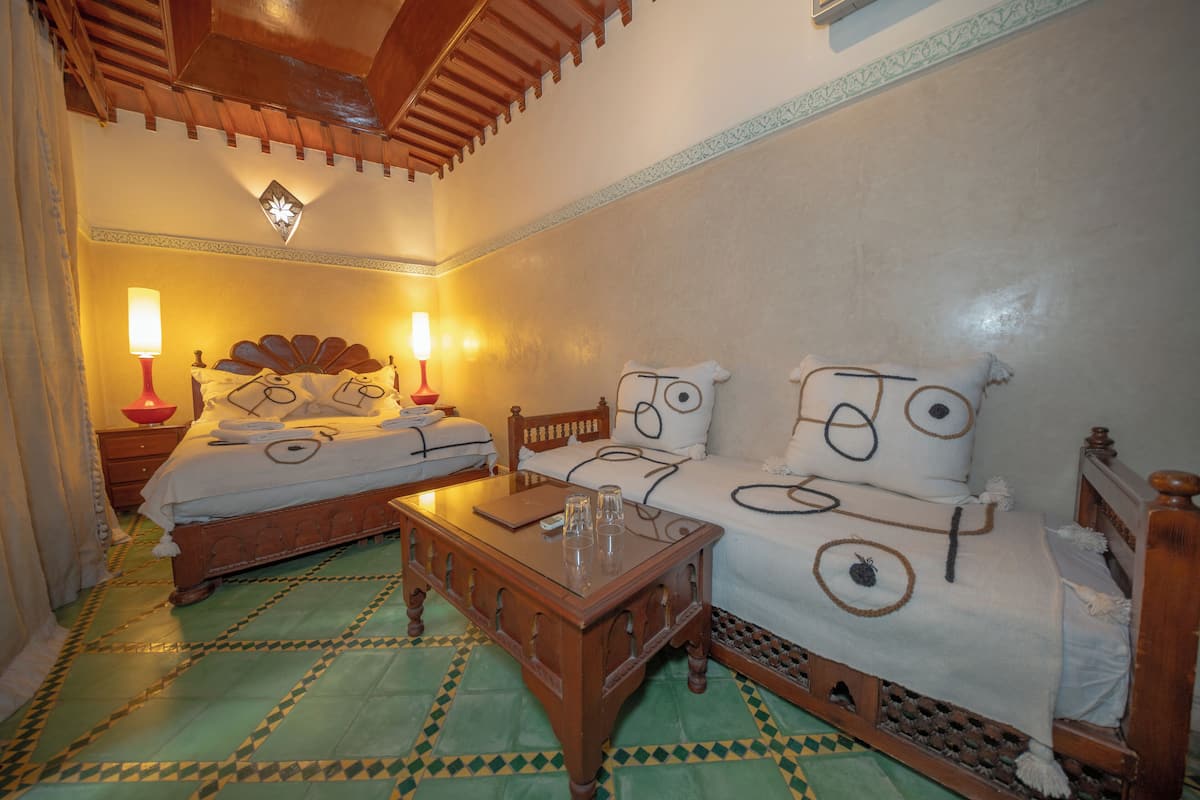 Une chambre avec deux lits, une table en bois et des carreaux de sol à motifs.