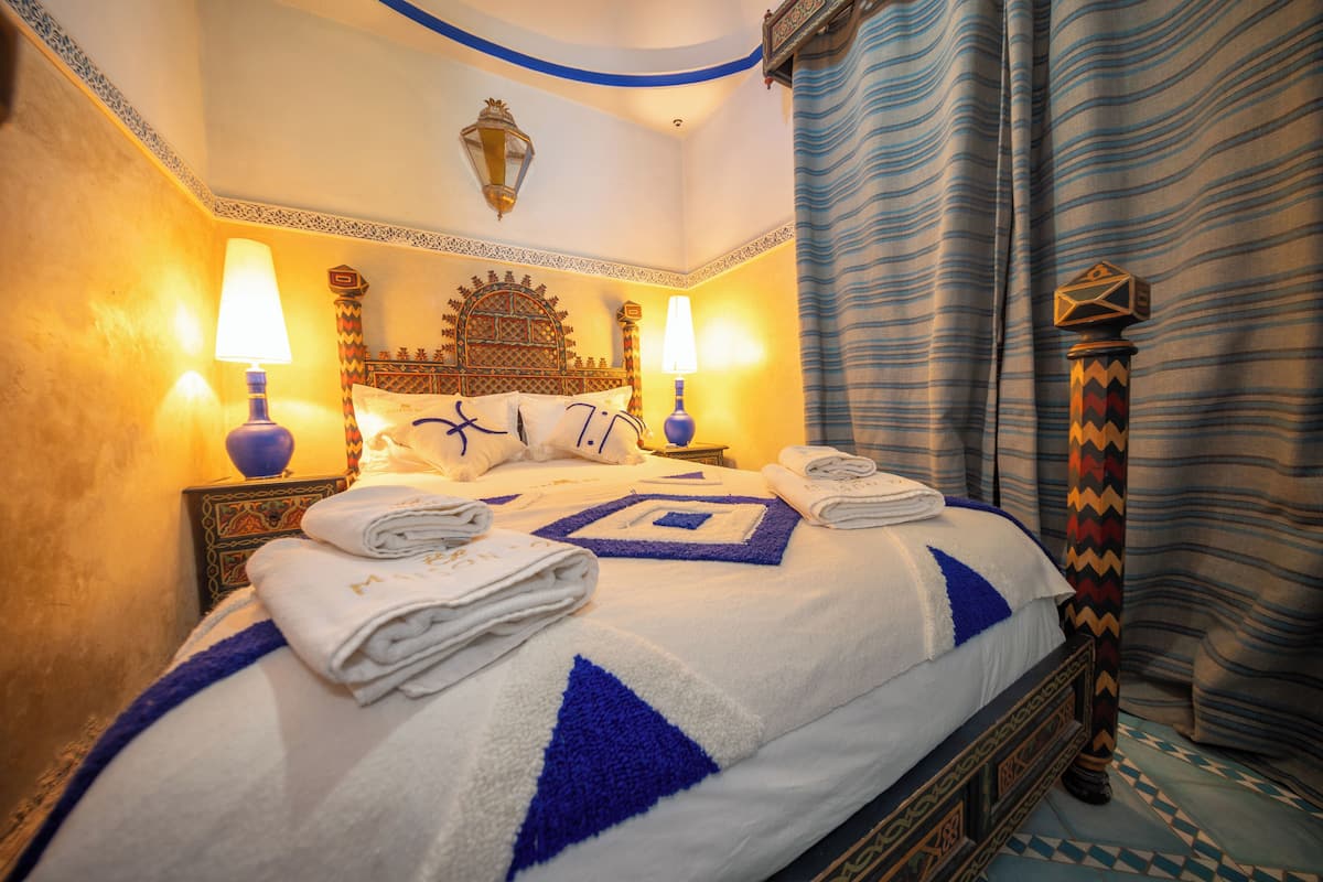 Un lit bien fait, agrémenté de serviettes, d’une tête de lit décorative et de deux lampes fixées au mur.
