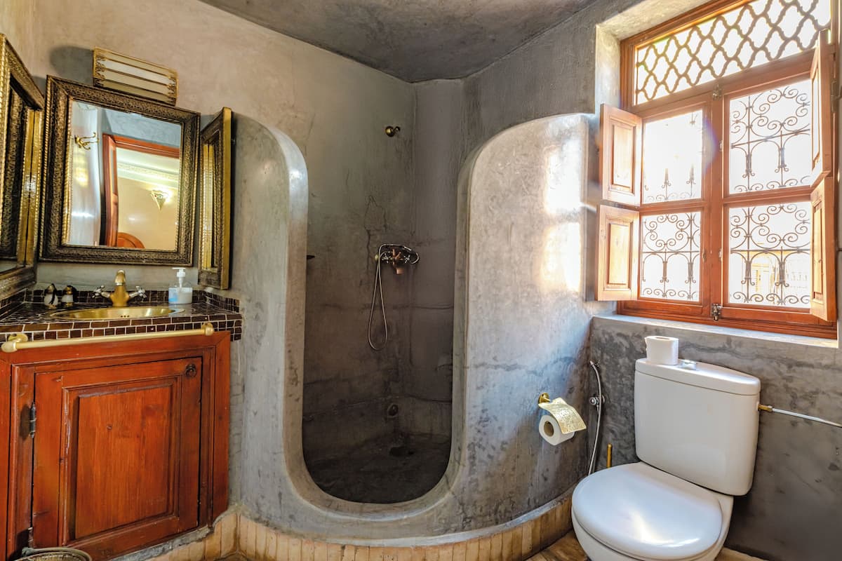 Une salle de bain équipée d’une baignoire, de toilettes et d’une fenêtre ornée de barreaux en fer décoratifs.