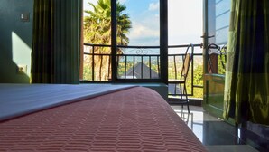 Un dormitorio con un ventanal grande, una cama, una silla y vistas a palmeras y una casa.