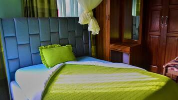 Una cama con cabecera capitonada, almohada verde y manta a rayas.