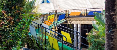 Un parque infantil lleno de color con toboganes y un pequeño puente, rodeado de exuberante vegetación y un edificio con tejado de baldosas.
