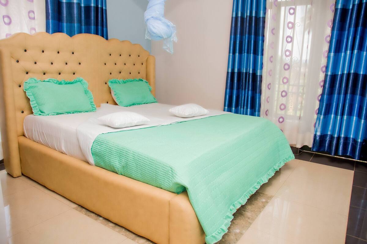 Una cama con cabecera acolchada, dos almohadas y una colcha verde.