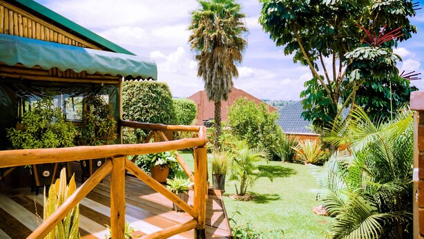Una terraza de madera con barandilla, rodeada de exuberante follaje y diversas plantas.