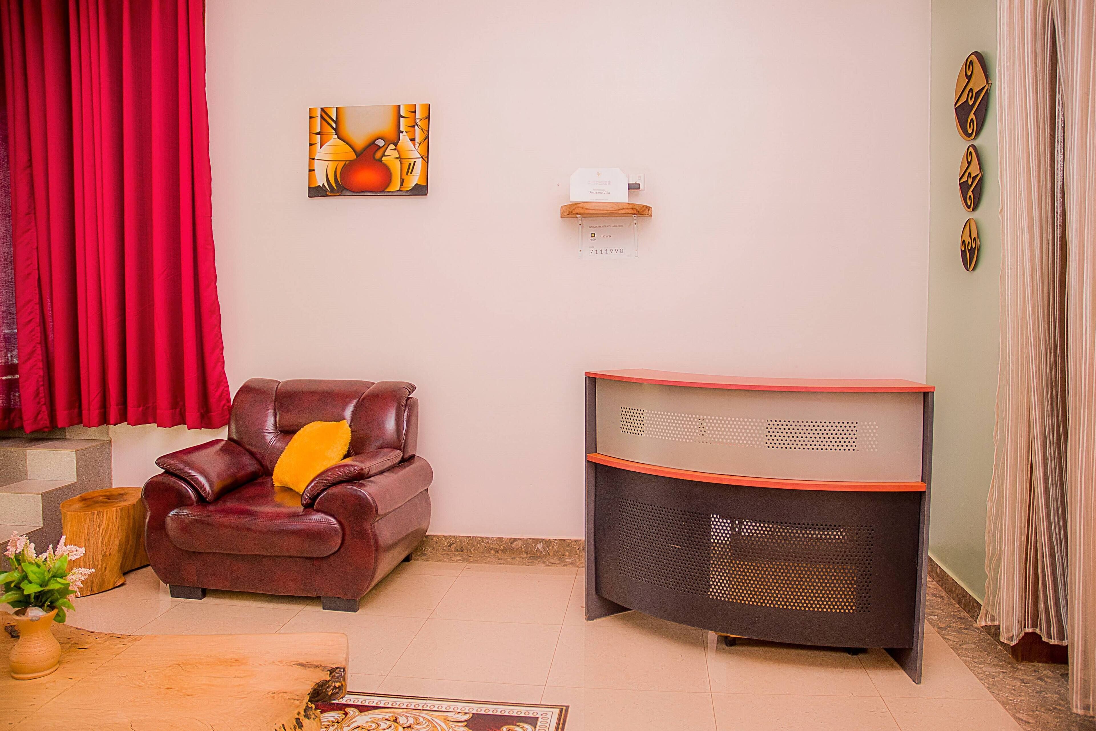 A living room with a leather sofa, a wooden coffee table, a red curtain, a painting, and a wall-mounted shelf.