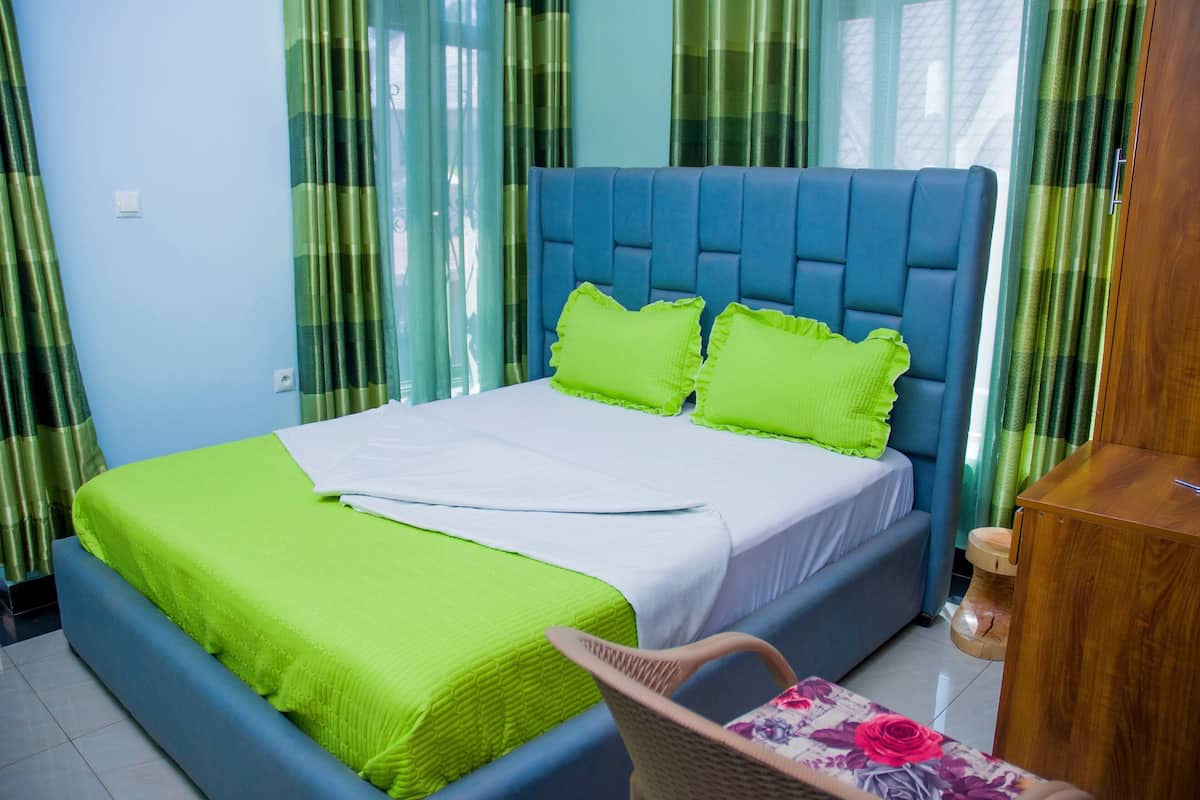 Una cama con cabecera azul, ropa de cama verde y una mesita de noche de madera.
