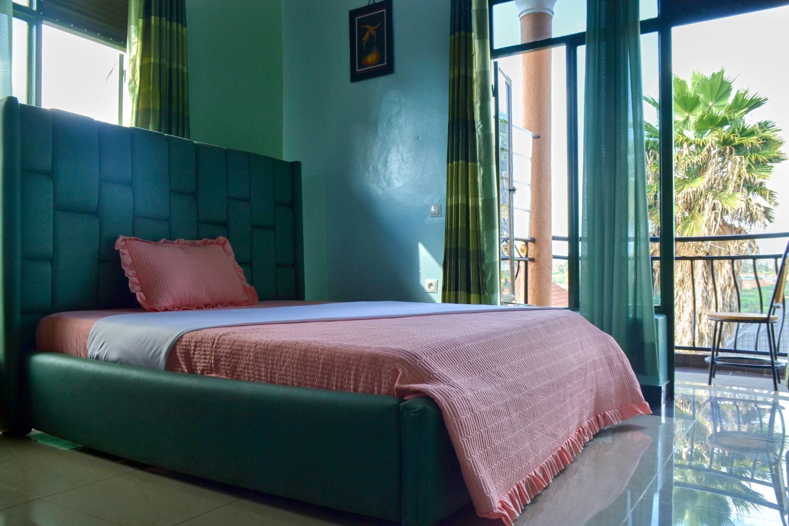 Un dormitorio con una cama grande, cabecera verde y vistas a palmeras a través de un balcón.