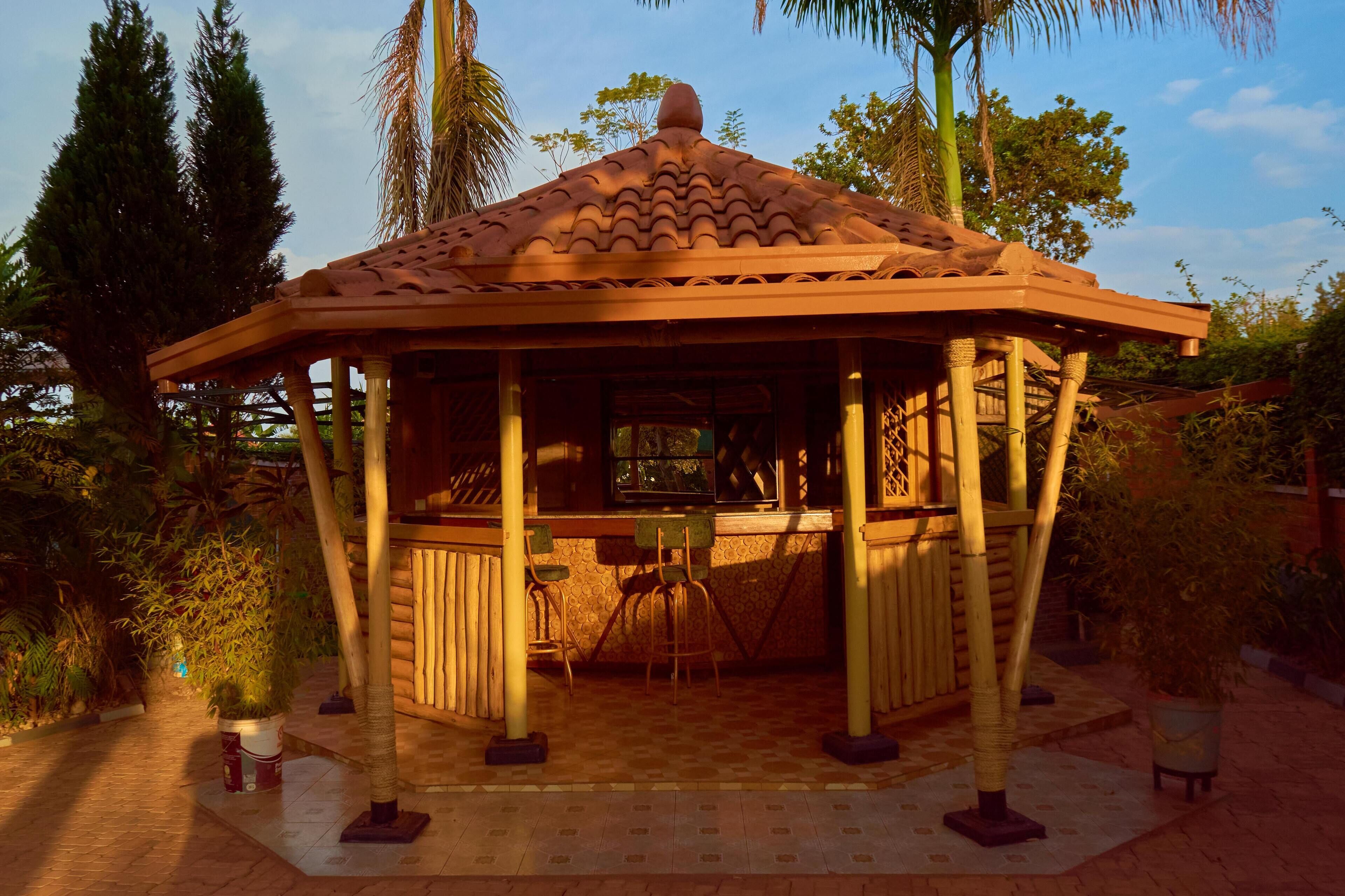 A gazebo with a tiled roof, wooden pillars, and a central table with chairs.