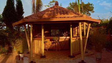 A gazebo with a tiled roof, wooden pillars, and a central table with chairs.