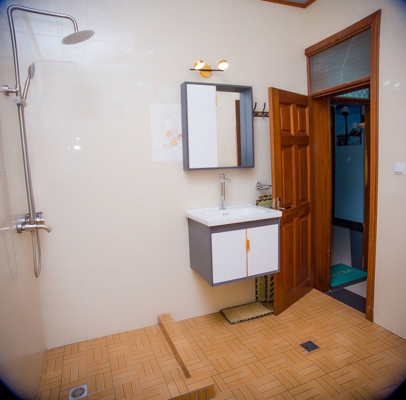 A bathroom with a shower, sink, mirror, and wooden door.