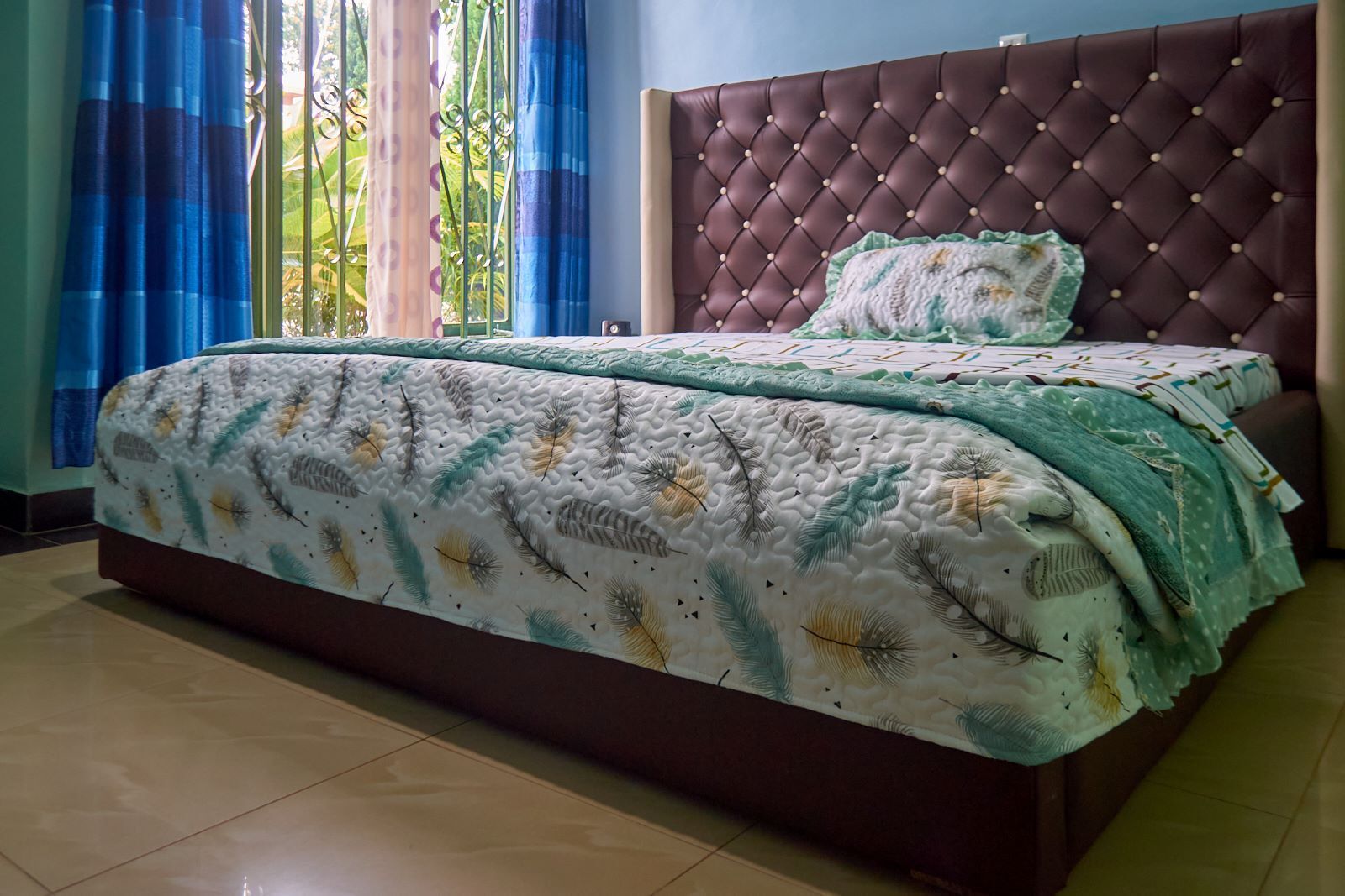 A bedroom with a tufted headboard, a large bed with patterned bedding, and curtains.