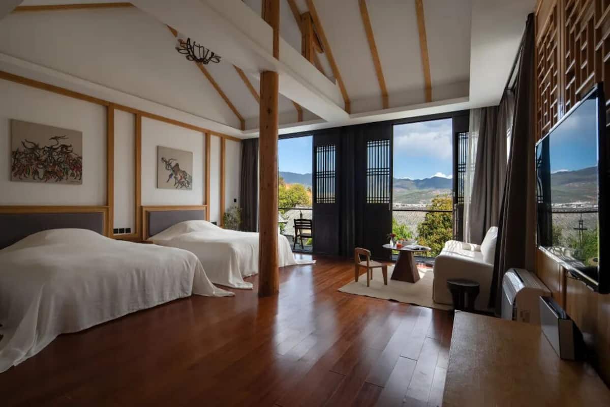 Ein Zimmer mit zwei Betten, Holzboden, großen Fenstern mit Bergblick und einem Sitzplatz auf dem Balkon.