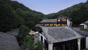 A traditional building with a curved roof, surrounded by lush greenery and hills. - GRAND JOLI (Lijiang)