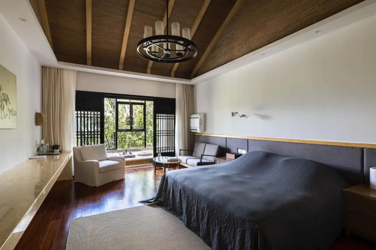 Ein modernes Schlafzimmer mit einem großen Bett, einer Holzbalkendecke und Blick auf Grünfläche.