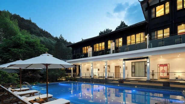 A modern hotel with a swimming pool, lounge chairs, and a traditional building with illuminated windows. - GRAND JOLI (Lijiang)