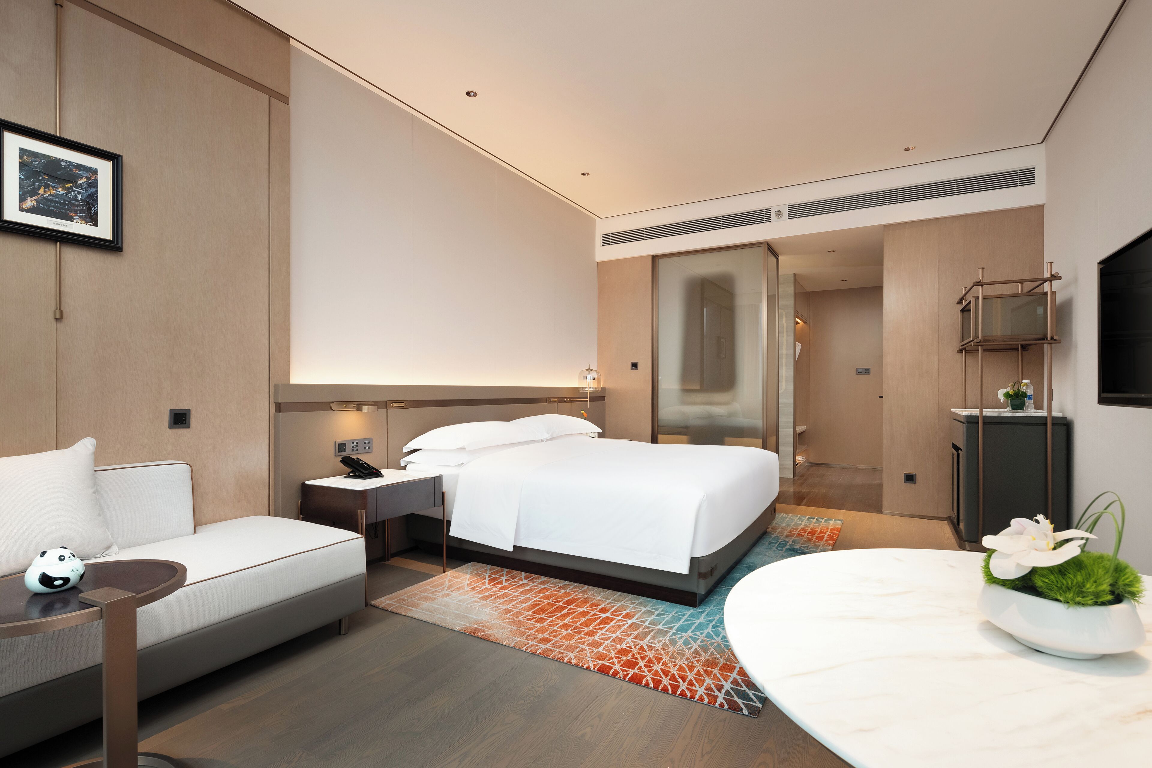 Quarto de hotel moderno com cama, mesa de cabeceira e um pequeno sofá.