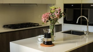 A modern kitchen with a white countertop, a coffee maker, a vase with flowers, and a sink. - Casa do Cruzeiro (Cascais)
