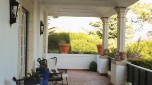 A covered outdoor area with a tiled floor, several wicker chairs, and potted plants. - Casa do Cruzeiro (Cascais)
