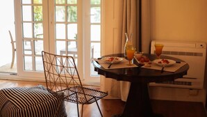 A dining area with a table set for two, a chair, and a view of the outdoors through a window. - Casa do Cruzeiro (Cascais)