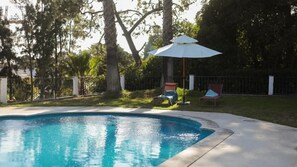 Una piscina con dos sillas de descanso y una sombrilla.