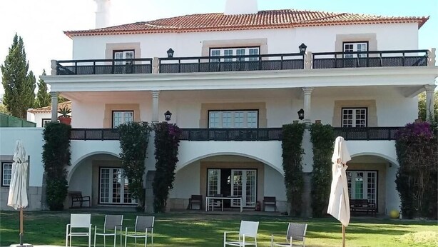 A large white building with a tiled roof, a swimming pool, and outdoor seating. - Casa do Cruzeiro (Cascais)