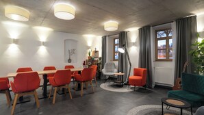 A modern dining area with a wooden table and orange chairs, a white armchair, and a green sofa. - dreamcation Altstadthotel Regensburg (Regensburg)