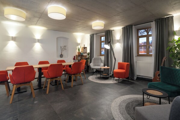 Un espace repas moderne avec une table en bois et des chaises orange, un fauteuil blanc et un canapé vert.