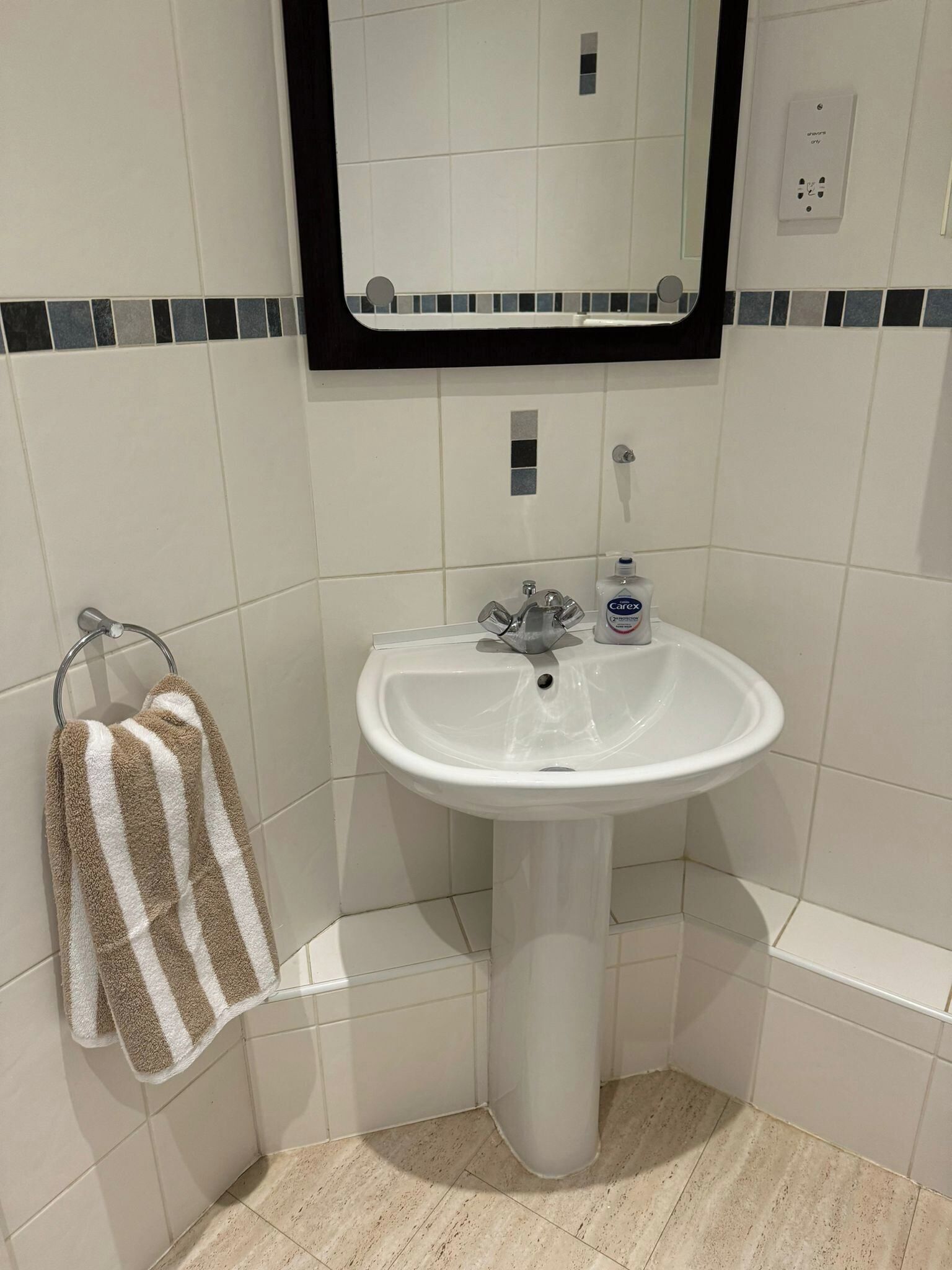 A bathroom with a white pedestal sink, a towel rack with striped towels, and a mirror with a black frame.