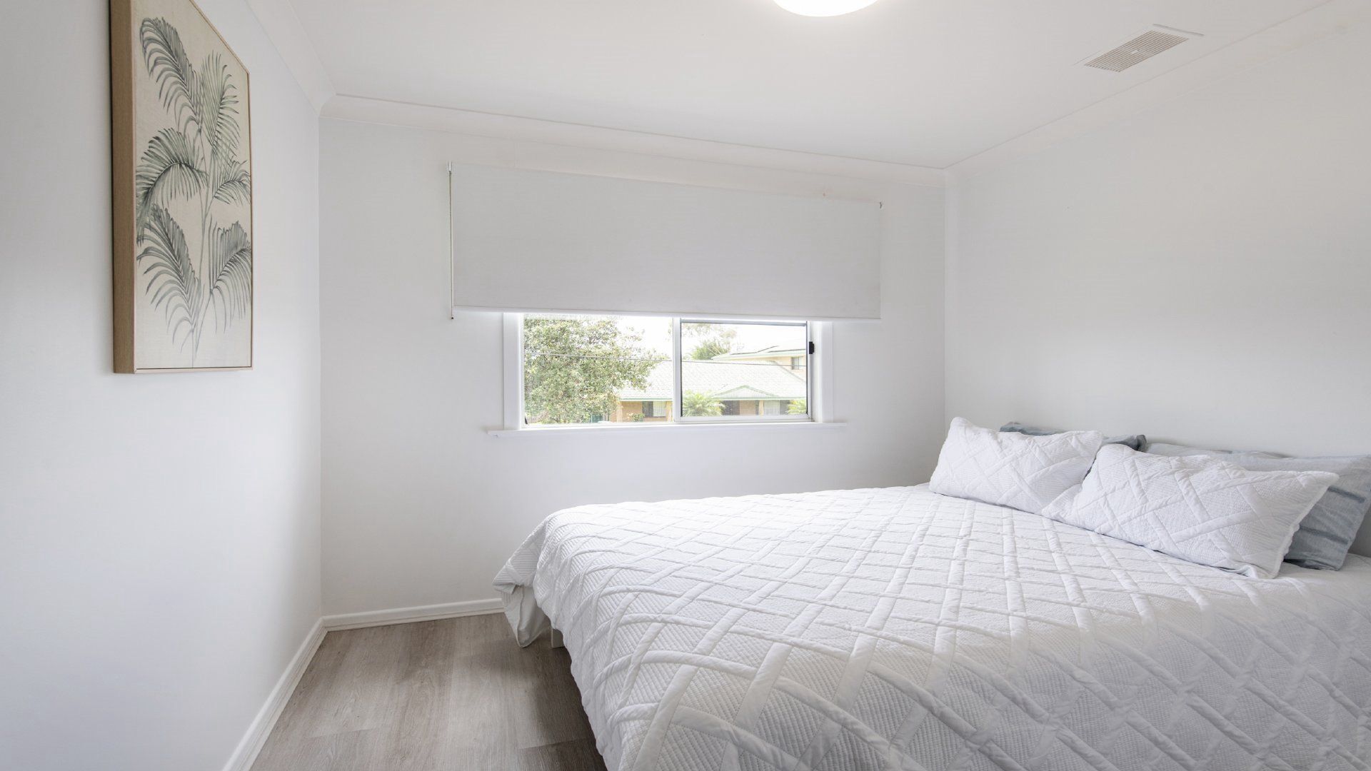 A bedroom with a bed, a window, and a wall-mounted artwork.