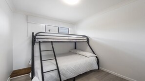 Een stapelbed met een ladder, witte beddengoed en een raam met uitzicht.