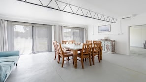 A dining area with a table and chairs, a sofa, a cabinet, and a large window with curtains.