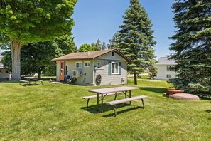 A small cabin with a picnic table in a grassy area, surrounded by trees.
