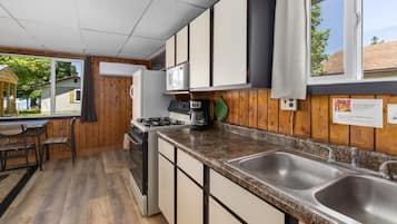 Una cocina compacta con armarios de madera, estufa a gas, microondas y pileta doble.