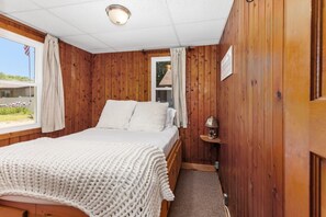 Habitación con paneles de madera, una cama, una mesita de noche y una ventana con cortinas.