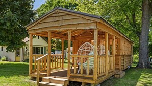Une cabane en bois dotée d’une véranda, de marches et d’un grand fauteuil en osier.