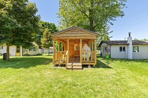 Eine hölzerne Laube mit Veranda, umgeben von einer Rasenfläche und Bäumen.