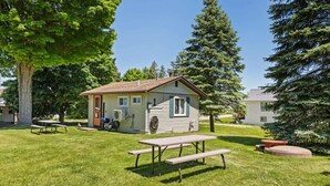 Une petite cabane avec une table de pique-nique, située dans un espace verdoyant et entourée d’arbres.