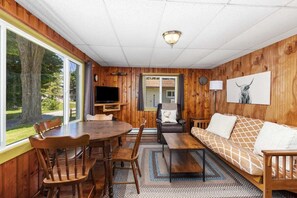Ein gemütliches Blockhaushaus-Interieur mit einem Holzespeisetisch, Stühlen, einer Couch und einem Fernseher.