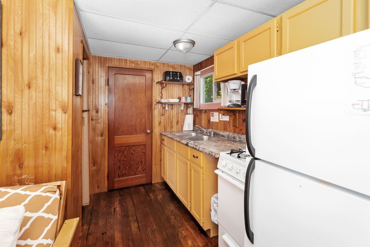 Una cocina compacta con paredes de madera, un refrigerador blanco, una estufa y un lavamanos.