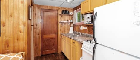Una cocina compacta con paredes de madera, un refrigerador blanco, una estufa y un lavamanos.