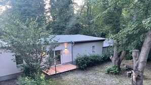 Una piccola casa moderna con tetto rosso e patio recintato, immersa nel verde.