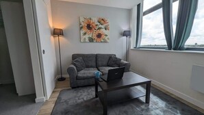 A modern living room with a gray sofa, a coffee table, a laptop, a floor lamp, and a painting of sunflowers on the wall.