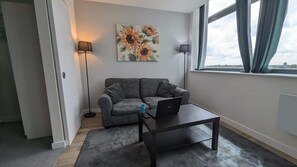 A modern living room with a gray sofa, a coffee table, a laptop, a floor lamp, and a painting of sunflowers on the wall.