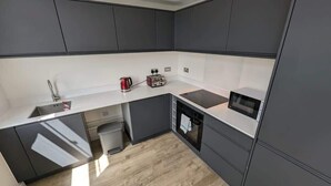 A compact kitchen with grey cabinets, a white countertop, a built-in microwave, and a kettle.